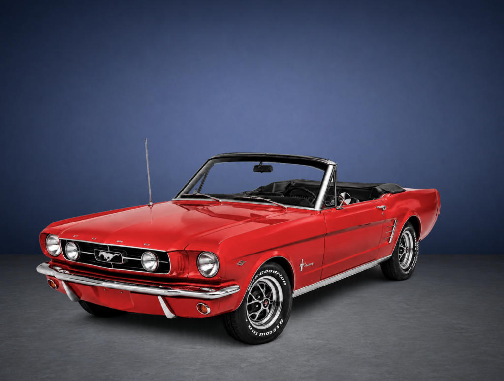 Red vintage Ford Mustang convertible with the top down against a dark blue studio backdrop, front-left view...